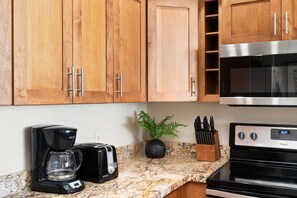 A kitchen with wooden cabinets, a stainless steel microwave, a black coffee maker, a toaster, a knife block, and a potted plant. - Ocean View 1BD Walk to Napili Bay Beach & Oceanfront Pools- Napili Point B38 (Lahaina)