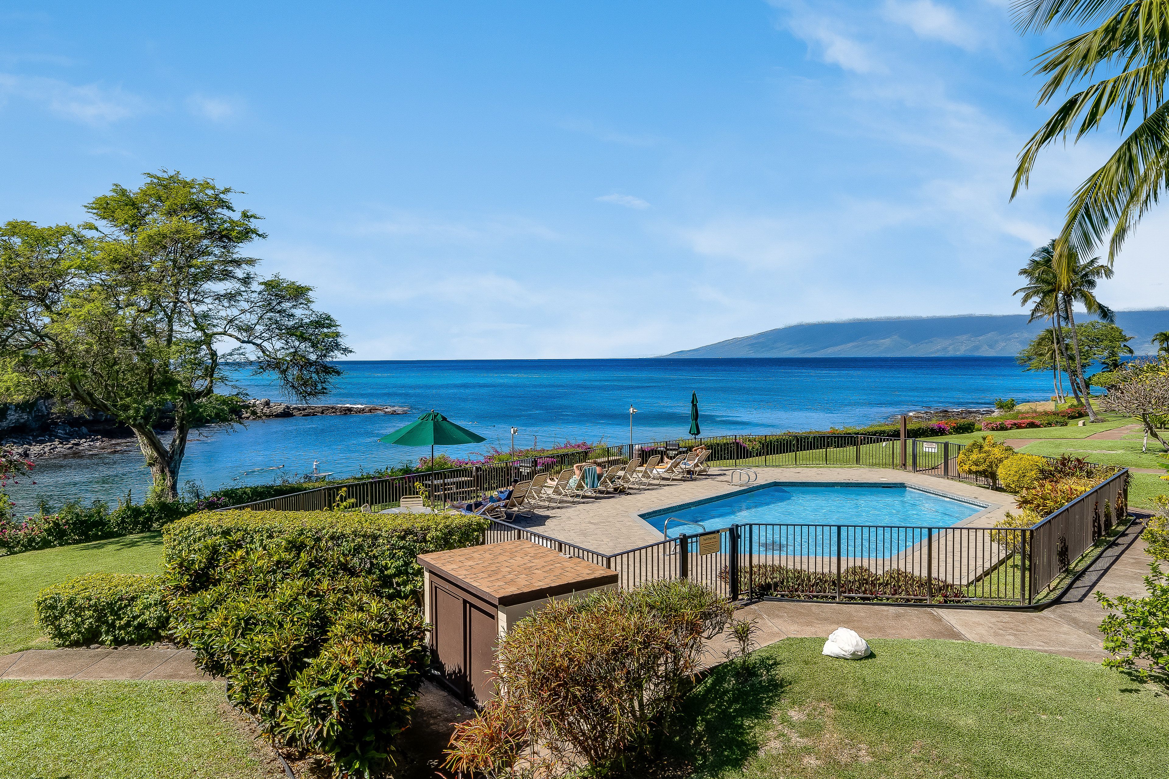 Une piscine avec vue sur l’océan, entourée d’une clôture, et un petit bâtiment en premier plan.