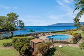 A pool with a view of the ocean, surrounded by a fence, and a small building in the foreground. - Ocean View 1BD Walk to Napili Bay Beach & Oceanfront Pools- Napili Point B38 (Lahaina)