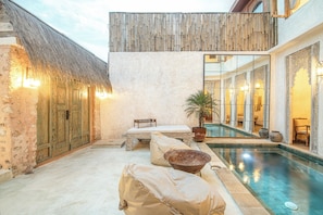 Uma área de piscina com um telhado de palha, um banco e uma espreguiçadeira.