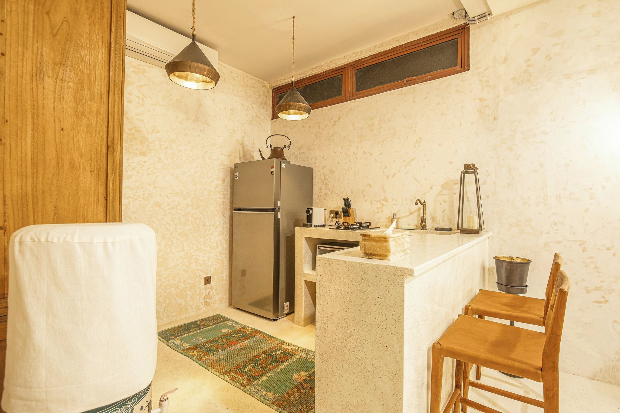 A compact kitchen with a refrigerator, a sink, a wooden chair, and a small table.