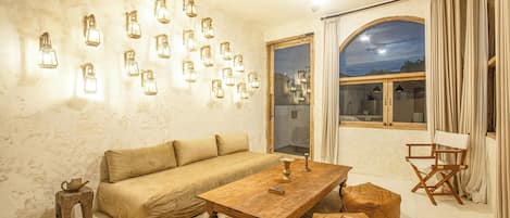 Un salon chaleureux avec un canapé, une table basse, des poufs et des lampes fixées au mur.