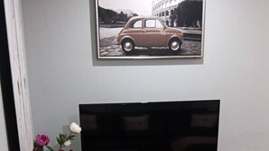 Un salon avec un téléviseur à écran plat posé sur un meuble blanc, un vase rempli de fleurs et un tableau encadré au-dessus du téléviseur.