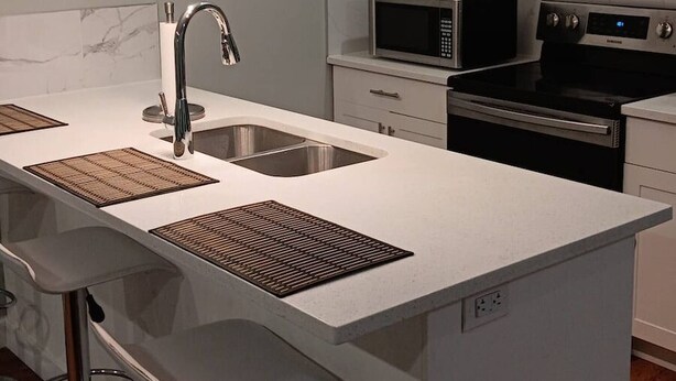 Une cuisine moderne dotée d’un îlot central, d’appareils électroménagers en acier inoxydable et d’une fenêtre avec des stores.