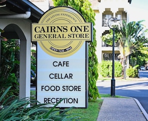 Schild für den Cairns One General Store mit Auflistung der Einrichtungen: Café, Weinkeller, Lebensmittelgeschäft und Rezeption.