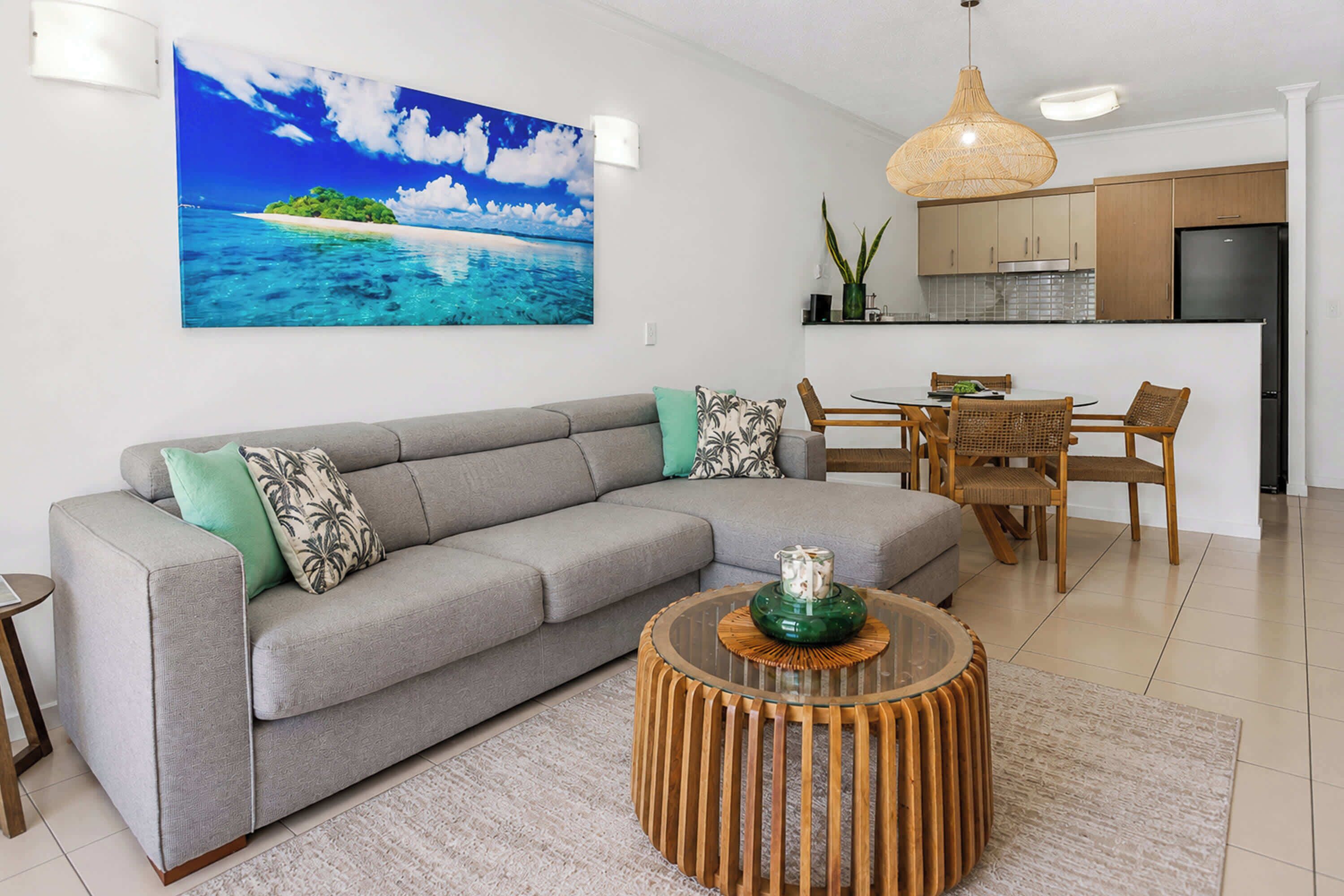 Ein modernes Wohnzimmer mit einem grauen Sofa, einem runden Couchtisch aus Holz und einem Gemälde von einem tropischen Strand.
