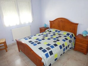 A bedroom with a wooden bed, a nightstand, a lamp, and a radiator. - Villa Alzina with Private Pool (L'Escala)