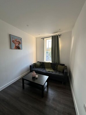 A modern living room with a dark-colored sofa, a coffee table, and a painting on the wall. - Stylish Two-Bedroom Flat (London)