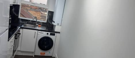 Une cuisine compacte équipée d’un lave-linge, d’une fenêtre et offrant une vue sur les bâtiments environnants.