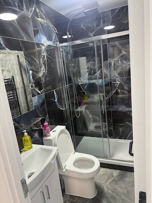 A bathroom with a white toilet, a sink, and a shower area. - Stylish Two-Bedroom Flat (London)