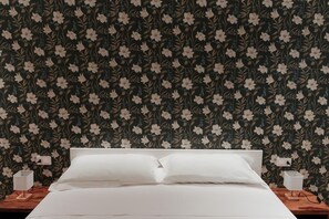 Ein Bett mit weißen Laken, einem Holzkopfschild und zwei Nachttischen mit Lampen.