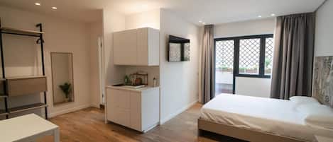 A modern bedroom with a bed, a small kitchenette, and a desk.