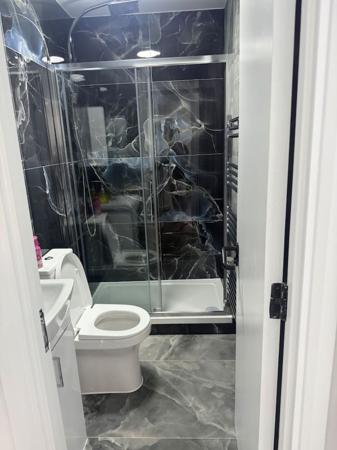 A bathroom with a glass shower enclosure, a toilet, and a sink.