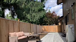 Ein Patio mit einer Rattan-Couch, einem kleinen Tisch und einer weißen Klimaanlage.