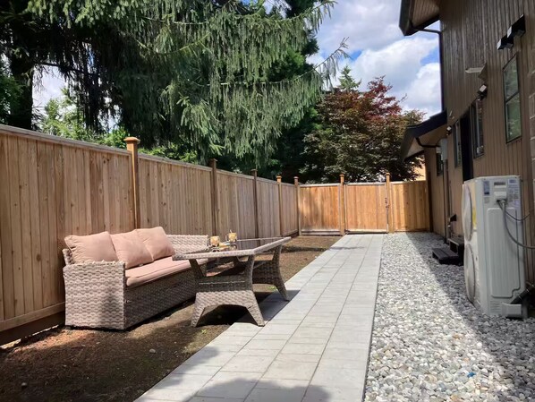 Un espace patio aménagé avec un canapé en osier, une petite table et un climatiseur blanc.