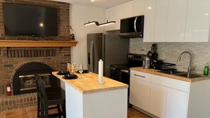 A modern kitchen with a central island, a flat-screen TV mounted on a brick wall, and a built-in microwave.