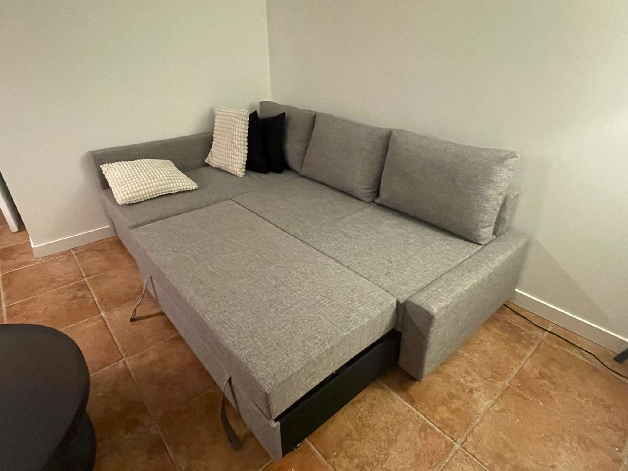 A grey sofa with a matching cover, a black chair, and a white cushion.