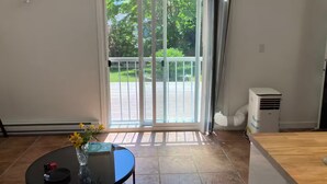 Ein Zimmer mit einer Schiebetür zum Balkon, einem runden Tisch mit einer Vase und einem Buch sowie einer weißen Klimaanlage.