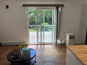 A room with a sliding glass door leading to a balcony, a round table with a vase and a book, and a white air conditioning unit.