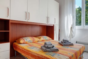 A bedroom with a bed, two pillows, a window with curtains, and a radiator. - Casa Medicea del Porto (Livorno)