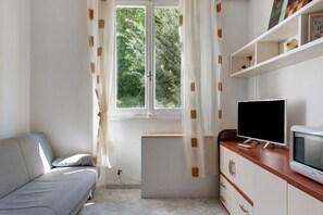 A room with a sofa, a television, a cabinet, and a window with curtains. - Casa Medicea del Porto (Livorno)