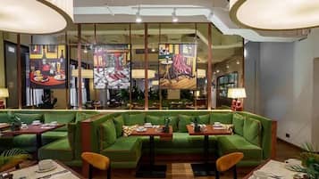 A restaurant with green upholstered seating, wooden tables, and artwork on the walls.