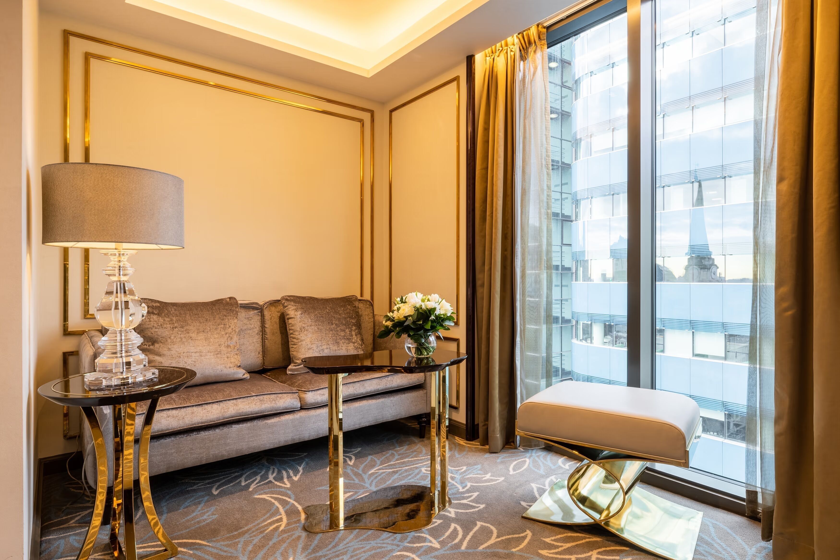 Habitación de hotel moderna con sofá, una mesita auxiliar, lámpara y vistas a un edificio a través de amplias ventanas.