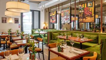 A restaurant interior with green upholstered booths, wooden tables, and hanging pendant lights.