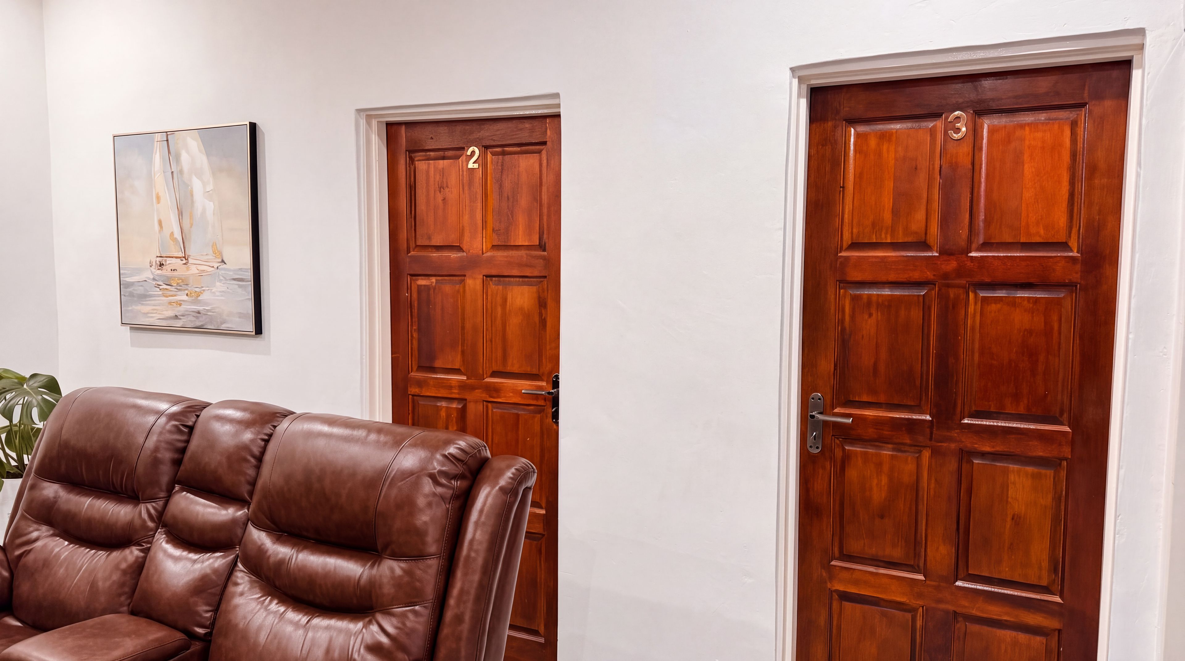 Een kamer met een bruine leren fauteuil, twee houten deuren met nummers en een schilderij in een lijst aan de muur.