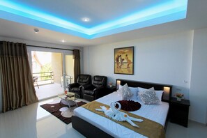 A modern hotel room with a large bed, two black leather chairs, a glass coffee table, and a painting on the wall.