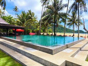 A swimming pool with a clear blue water, surrounded by palm trees and a beach in the background. - Siam Royal View Resort Apartment #1120 (Ko Chang)