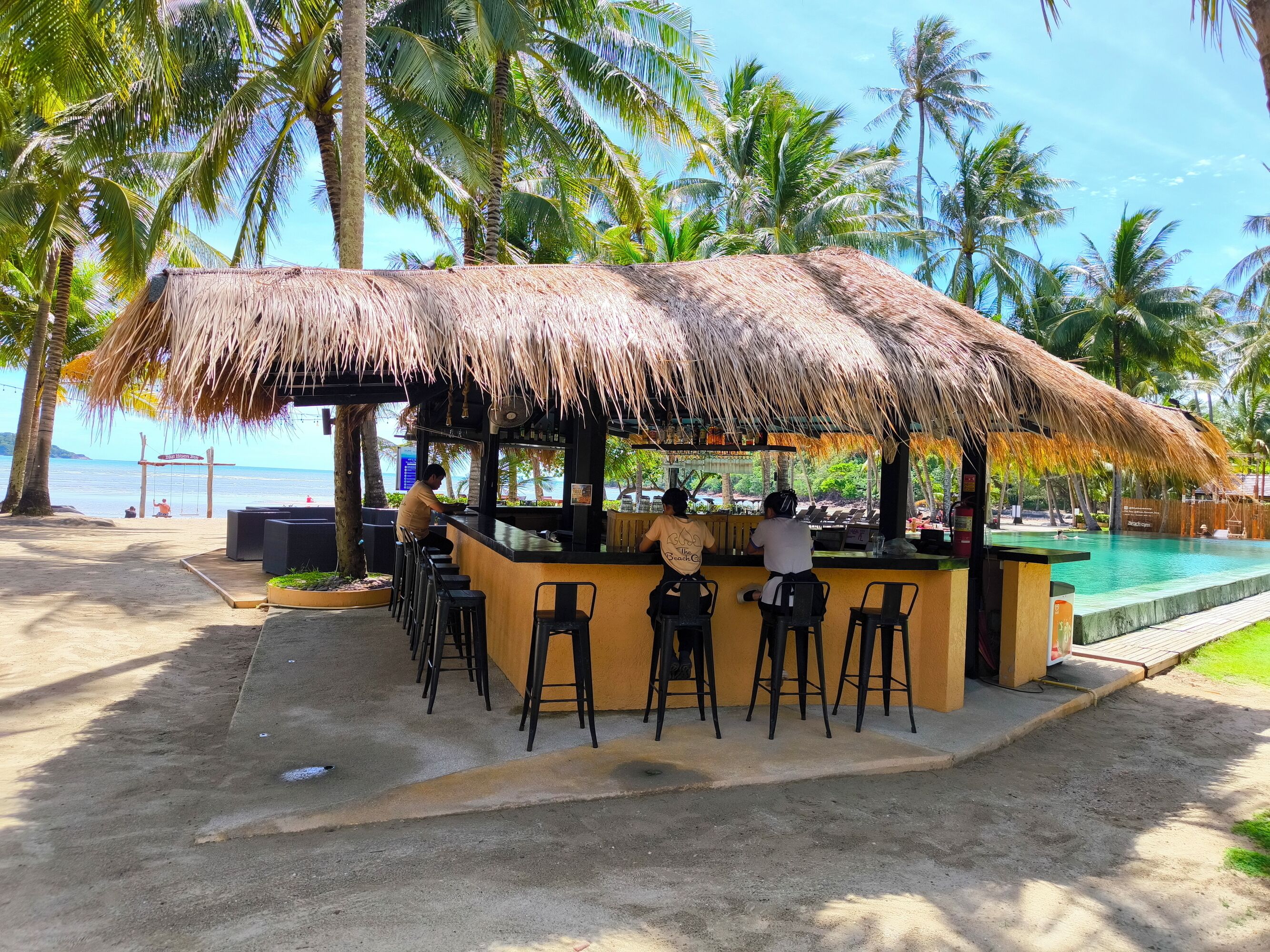 A beachside bar with a thatched roof, outdoor seating, and a view of the ocean.