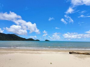 A beach with clear skies, calm waters, and a distant island.