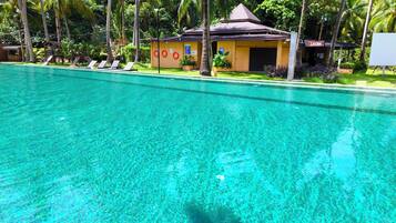 A clear swimming pool with lounge chairs and a small building with a sign that reads 'SAUNA'.