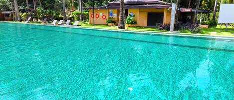 A clear swimming pool with lounge chairs and a small building with a sign that reads 'SAUNA'.