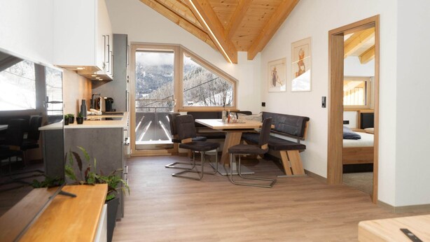 En modern inredning med matplats, kök och utsikt över snöklädda berg.