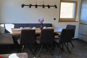 Ein Essbereich mit Holztisch, vier Stühlen, einer Blumenvase und einem Fenster mit Jalousien.