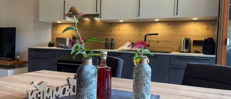 A modern kitchen with wooden cabinets, a dining table with a placemat, and two decorative vases with flowers.