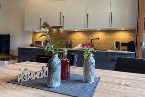 A modern kitchen with wooden cabinets, a dining table with a placemat, and two decorative vases with flowers. - Panoramic view apartment Kaunergrat (Kaunerberg)