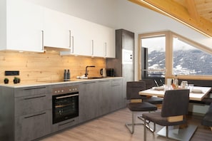 Eine moderne Küche mit Einbauofen, Essbereich mit Tisch und Stühlen sowie ein großes Fenster mit Blick auf eine verschneite Landschaft.