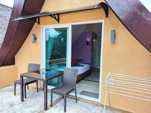 A room with a glass door leading to a balcony, wicker furniture, and a bed with a purple wall. - 4 Bedroom Deluxe Beach Villa 21C, Blue Haven Bay Resort (Ko Chang)