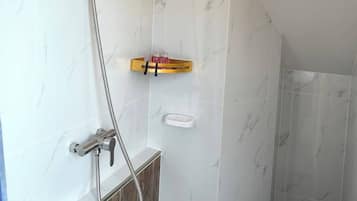 A bathroom with a shower, a wooden vanity, and a marble-tiled wall.