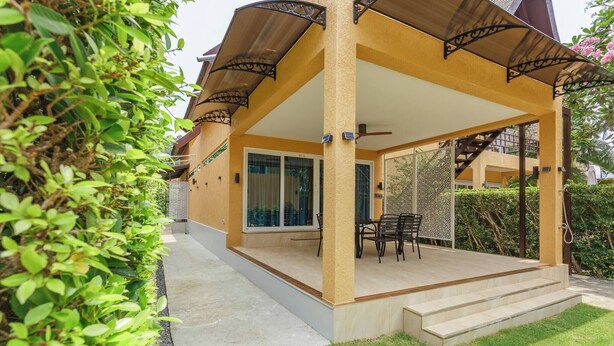 A covered outdoor area with a table and chairs, a staircase leading to an upper level, and a view of a building in the background. - Beach Villa 21D Blue Haven Bay Resort - 4 rooms (Ko Chang)
