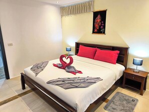 Een netjes opgemaakt bed met een rode en grijze handdoekenset, een houten hoofdbord en een aan de muur bevestigd kunstwerk.