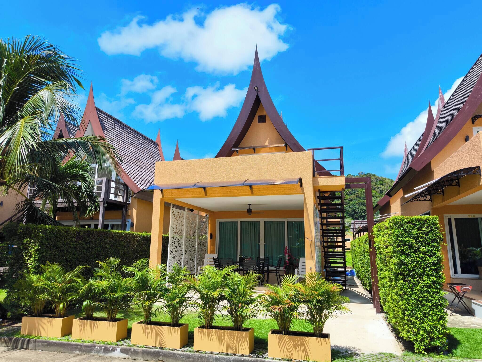 A hotel with a traditional architectural style, featuring a central atrium with a staircase, surrounded by lush greenery and palm trees.