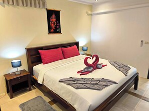 Habitación de hotel con cama, almohadas, mesita de noche con lámpara, una obra de arte en la pared y una puerta.