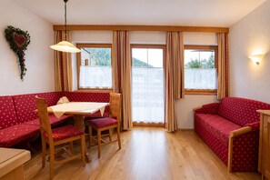 A cozy room with a wooden floor, a red sofa, a wooden dining table with chairs, and a window with curtains. - Tyrolean Apartment with Terrace (Achenkirch)