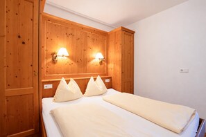 A hotel room with wooden paneling, two bedside lamps, a bed with white linens, and a wall socket. - Tyrolean Apartment with Terrace (Achenkirch)