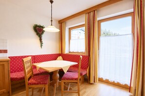 A dining area with a wooden table and chairs, a bench with red cushions, and a window with curtains. - Tyrolean Apartment with Terrace (Achenkirch)