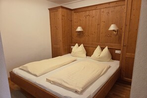 Una cama doble con dos almohadas, cabecera de madera y dos lámparas de pared.